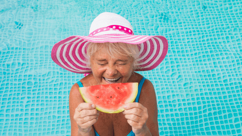 A woman in a pool holds up a slice of watermelon like it's a big smile
