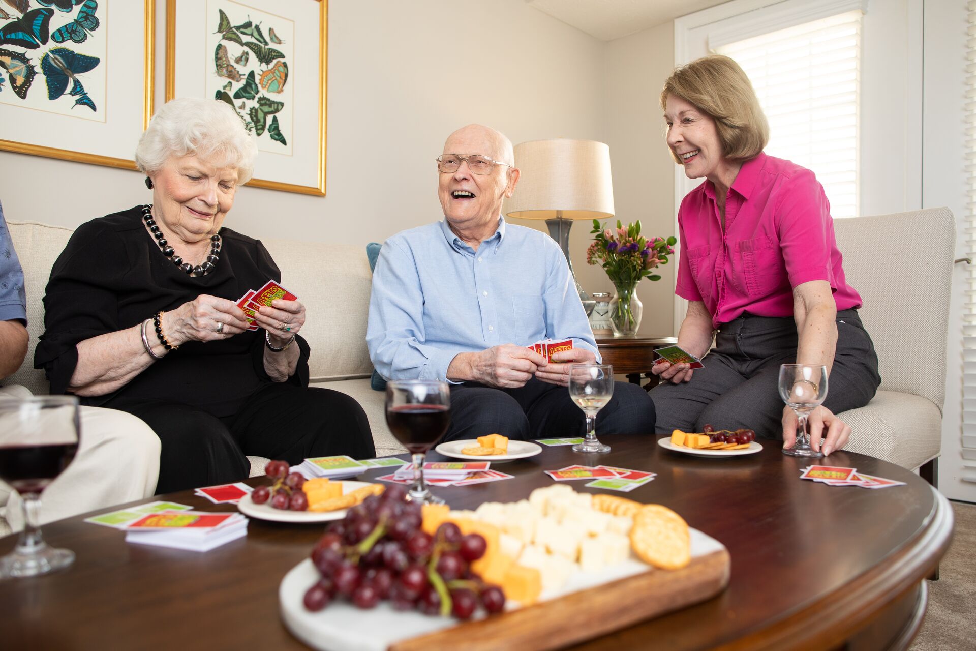 A group of seniors play cards and enjoy a charcuterie board.