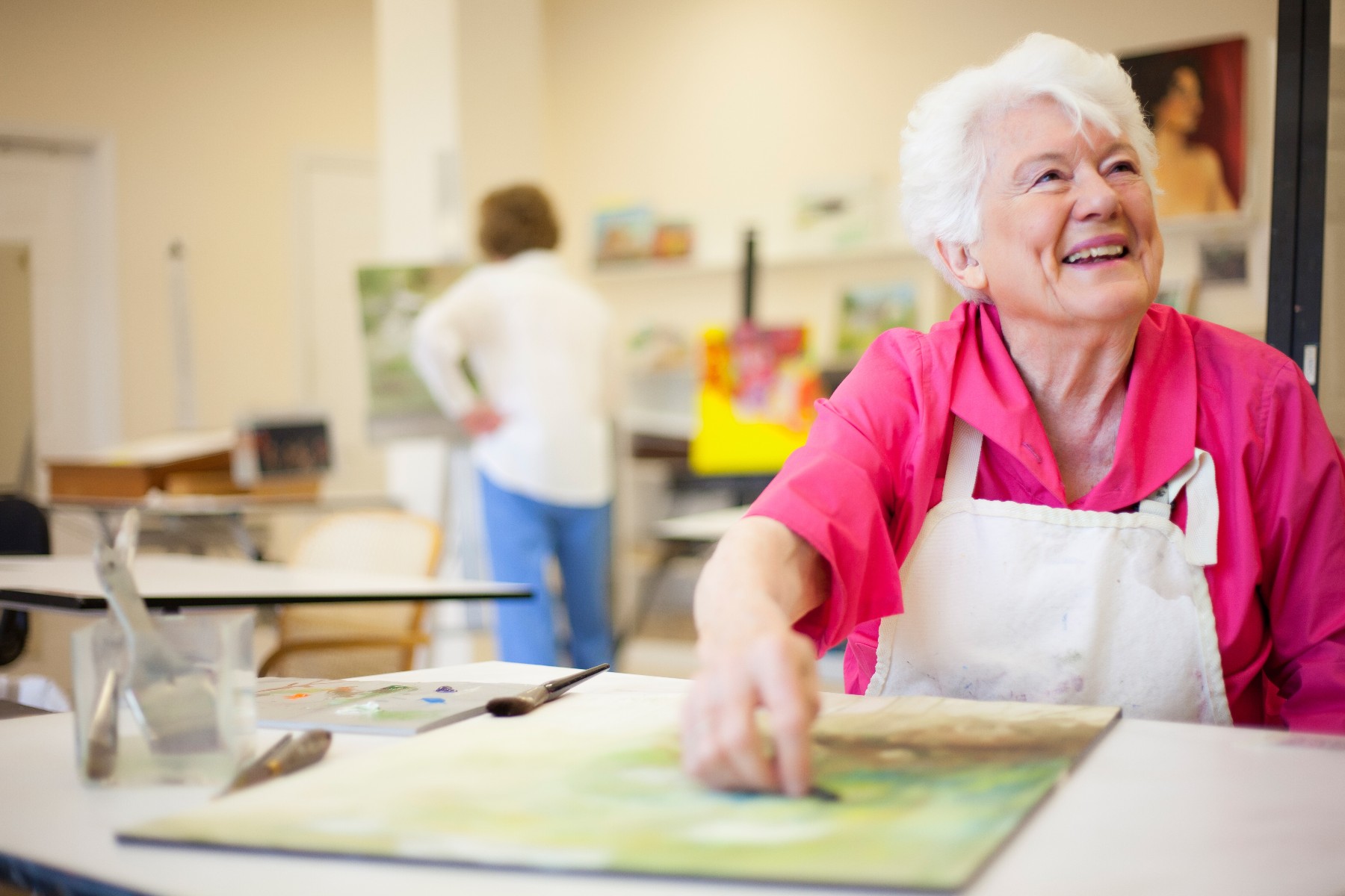 A smiling senior woman draws on a canvas in a bright and cheery art studio.