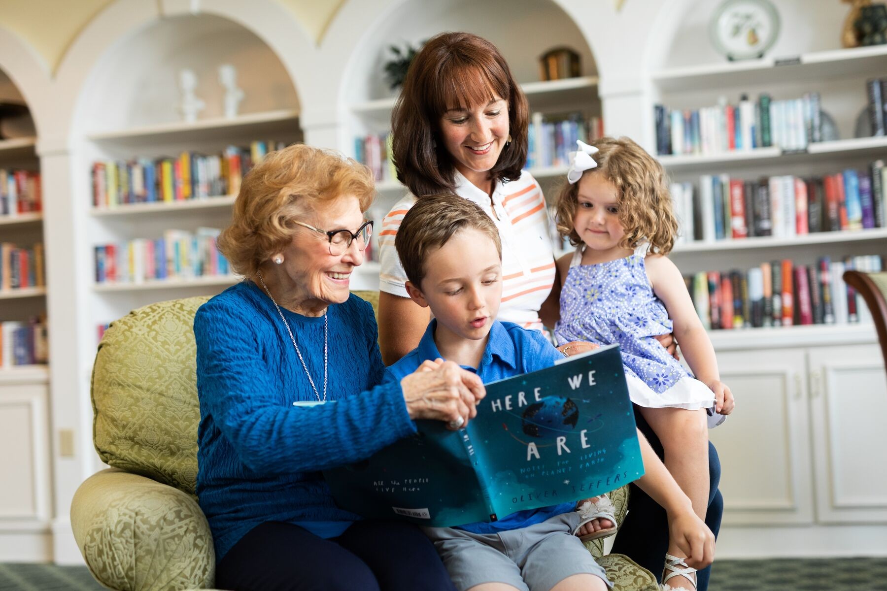 senior resident in library area reading a book with grandchildren and daughter