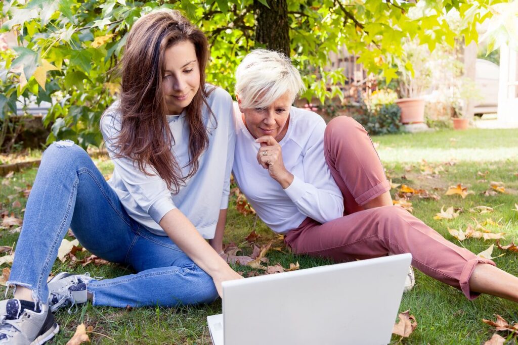 adult daugter and mom looking at laptop outside on grassy ground