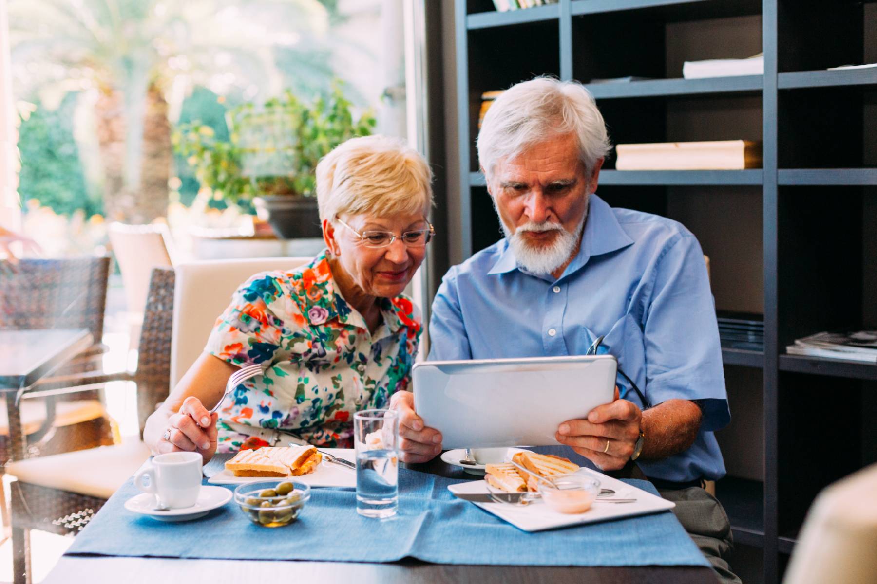 A senior couple enjoy breakfast and look at an ipad or tablet together